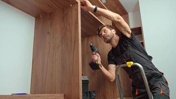 Man wearing work overalls assembling wooden wardrobe with drill and tools video