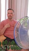A man tired of the heat rests under a fan in his house. Cooling helps him to feel better on a hot summer day. Home comfort concept, air conditioner manufacturers. video