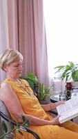 A lady wearing glasses tries to read a book in her apartment and has vision problems due to farsightedness and aging. Concept. care of the elderly, ophthalmology. video