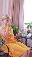 An elderly woman with glasses sits in her apartment and uses a smartphone. She communicates with her loved ones online and enjoys new technologies. Services for pensioners, mobile applications. video