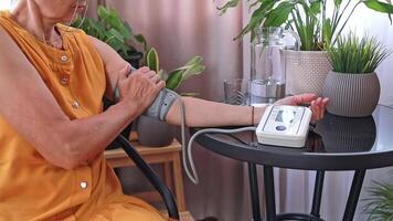 An elderly woman uses a tonometer to measure her blood pressure in her home. Taking care of her health is important to prevent chronic diseases. The concept of caring for the elderly. video