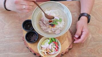 Close up of traditional Asian pho bo soup with noodles, beef, onion and chili pepper in a bowl. Travel, vacation, takeaway video