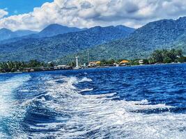 Island View From Ocean with Wake and Lush Green Mountains in Background photo