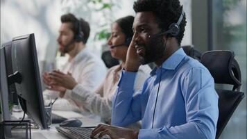 Multinational team African male callcenter operators thumbs up headset smiling office computer support female Indian coworker typing customer service happy Caucasian colleague job call center business video