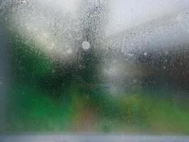 A wet window with a blurry image of a green grass photo