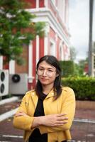 A woman with glasses and a yellow jacket standing in front of a building photo
