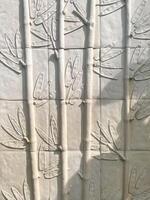 A wall with a lot of white tiles with leaves on them photo