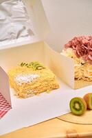 Luscious layered cake in white box with kiwi garnish and fresh flowers on wooden table photo
