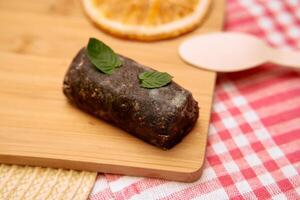Chocolate ganache log with mint leaves on wooden board with red gingham cloth photo
