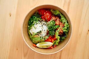 Healthy salmon poke bowl with fresh vegetables, avocado, and lime garnish on wooden table photo