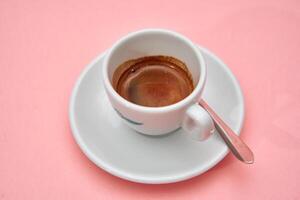 Fresh espresso coffee in white cup on pink background with silver spoon photo