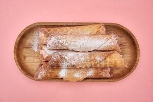 Delicious strawberry waffle rolls with powdered sugar on wooden platter photo