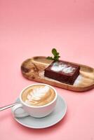 Cappuccino with latte art and chocolate cake on wooden tray against pink background photo