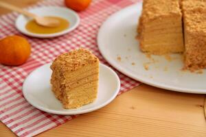 Layered honey cake with crumb topping on red checkered cloth featuring whole mandarin oranges photo