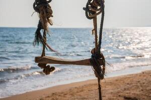 A swing hanging on the beach by the ocean photo