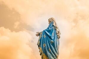 A statue of mary is standing in front of clouds photo