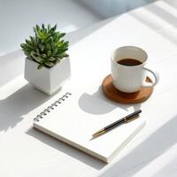 A coffee cup, pen and notepad on a white table with sunlight photo