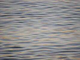 A tranquil close-up of gently rippling water illuminated by warm, golden light from a sunset. Wave pattern for wellness, nature, or background theme concepts photo