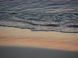 Gentle ocean waves lapping against the shore with wet sand. A serene coastal scene during golden hour. Background theme related to relaxation, mindfulness, travel, nature, and wellness photo