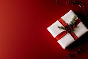 Holiday Present Wrapped in White Paper With Red Ribbon and Festive Greenery on a Red Background photo