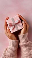 Gift Box Held in Hands With Soft Pink Background and Cozy Sweater photo
