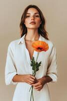 Woman Holding Vibrant Orange Flower While Dressed in a White Shirt Indoors. photo