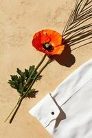 Bright Orange Poppy Flower With Greenery and a White Fabric on a Textured Surface photo