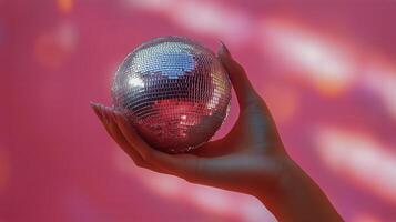 Hand Holding a Disco Ball Against a Pink Background With Soft Lighting Effects. photo