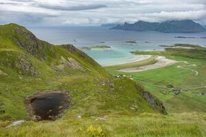 Small town in the valley near sandy ocean beach surrounded by mountains and hiddden peak pond viewed from Ryten hill, Lofoten Norway photo