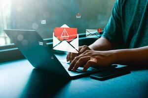 Cybersecurity threat concept showing a man using laptop with floating email icons containing malware warnings and danger signs, symbolizing phishing scam, virus attack, and online data security risk photo