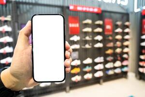 Hand Holding Blank Smartphone in Shoe Store. Mobile shopping for footwear, using retail apps, comparing prices online, or showcasing digital advertisements related to shoes. copy space. photo