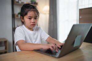 Young girl with concentrated expression typing on laptop at home workspace, showcasing focus and determination in a cozy learning environment photo