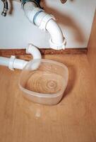 Close-up image showing a disconnected and leaking P-trap pipe beneath a bathroom sink photo