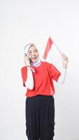Indonesia independence day celebration concept with excited Asian girl wearing red and white Indonesia flag color attribute talking on the phone call isolated on white background photo