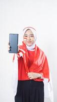 Indonesia independence day celebration with Asian girl wearing red and white Indonesia flag color attribute showing blank screen smartphone to camera isolated on white background photo