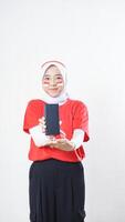 Indonesia independence day celebration with Asian girl wearing red and white Indonesia flag color attribute showing smartphone blank screen to camera isolated on white background photo