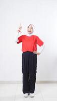 Excited Asian girl celebrate Indonesia independence day with red and white outfit raising her index finger to the up isolated on white background photo