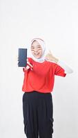 Indonesia independence day celebration with excited Asian girl wearing red and white Indonesia flag color attribute showing smartphone blank screen and her thumb up isolated on white background photo