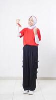 Excited Asian girl celebrate Indonesia independence day with red and white outfit showing winning gesture with raising both her clenched fists isolated on white background photo