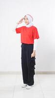 Side view of Asian girl celebrate Indonesia independence day with red and white outfit showing salute pose with raising her right hand to the eyebrow isolated on white background photo