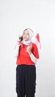 Indonesia independence day celebration with smiling Asian girl wearing red and white Indonesia flag color attribute talking on the phone call isolated on white background photo