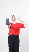 Indonesia independence day celebration with Asian girl wearing red and white Indonesia flag color attribute showing smartphone blank screen and OK sign hand gesture isolated on white background photo
