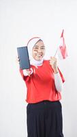 Indonesia independence day celebration with excited Asian girl wearing red and white Indonesia flag color attribute showing blank screen smartphone to camera isolated on white background photo
