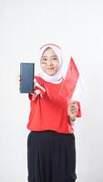Indonesia independence day celebration with beautiful Asian girl wearing red and white Indonesia flag color attribute showing blank screen smartphone to camera isolated on white background photo