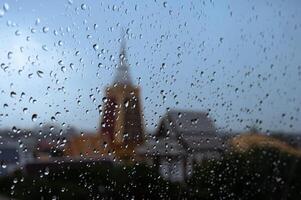 Rain drops on glass window in monsoon season with blurred temple building background. photo