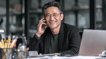 Asian businessman smiling talking on phone in modern office with laptop photo