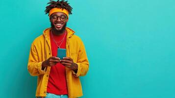 Joyful young man smiles while using his smartphone against a bright teal background, showcasing a vibrant and cheerful atmosphere photo