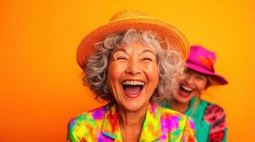 Two joyful older women in colorful outfits and hats laugh together against a vibrant orange background during a cheerful afternoon gathering photo