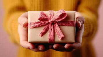 Beautifully wrapped gift held by hands in a cozy setting featuring a warm yellow sweater and pink backdrop, perfect for celebrations or special occasions photo
