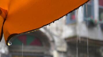 Rain droplets fall from an orange umbrella in a city setting video